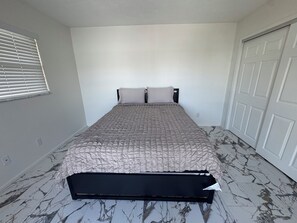 A bedroom with a bed, a window with blinds, a door, and a marble-patterned floor. - Tranquil 2-bedroom townhome with AC in charming Clewiston (Clewiston)