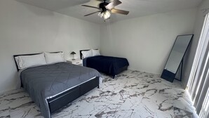 Una camera da letto con un letto matrimoniale, un letto singolo, una ventola a soffitto, uno specchio e un pavimento dal motivo marmorizzato.