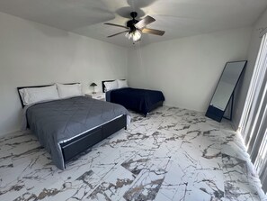 A bedroom with a bed, a smaller bed, a ceiling fan, a mirror, and a marble-patterned floor. - Tranquil 2-bedroom townhome with AC in charming Clewiston (Clewiston)