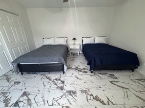 A bedroom with two beds, a white door, and a nightstand with a lamp. - Tranquil 2-bedroom townhome with AC in charming Clewiston (Clewiston)