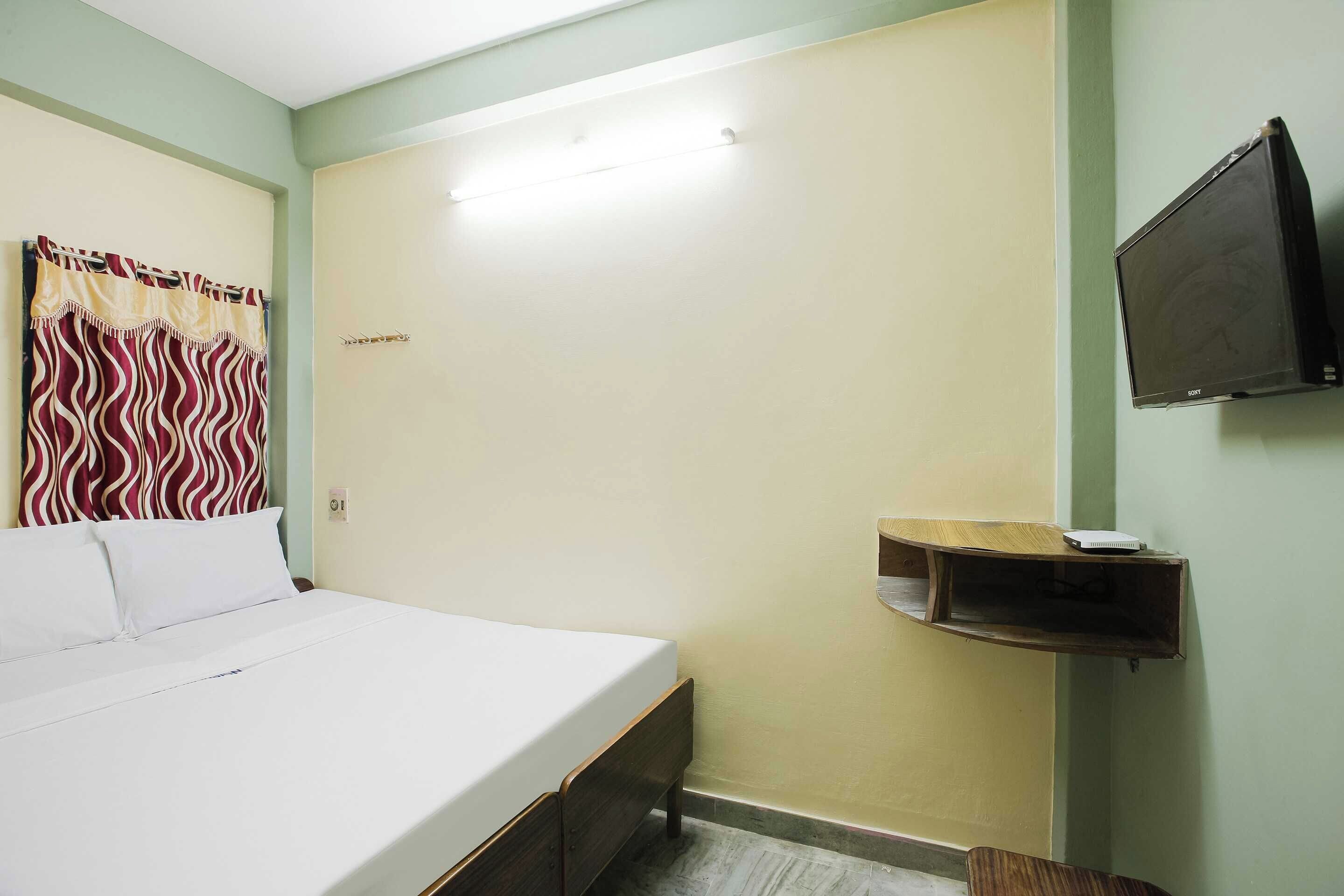 Una habitación de hotel con una cama, un televisor montado en la pared y un pequeño estante de madera.