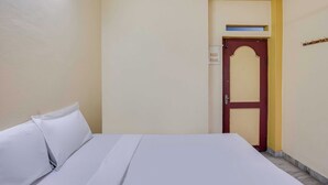 Hotellihuone, jossa on sänky, ovi ja seinään kiinnitetty valaisin.