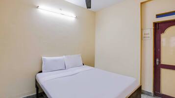 Una cama individual con ropa blanca en una habitación con paredes color crema y un ventilador de techo.