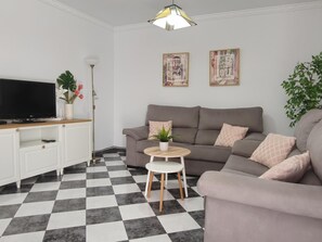 Un salon avec un canapé gris, une petite table ronde, un téléviseur posé sur un meuble et deux œuvres d’art accrochées au mur.