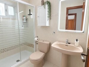 A bathroom with a glass shower enclosure, a toilet, a sink, and a mirror. - Nerja Sun Apartments Diputación 8 Center (Nerja)