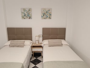 Une chambre double avec deux lits, une table de chevet, une lampe et deux œuvres d’art accrochées au mur.