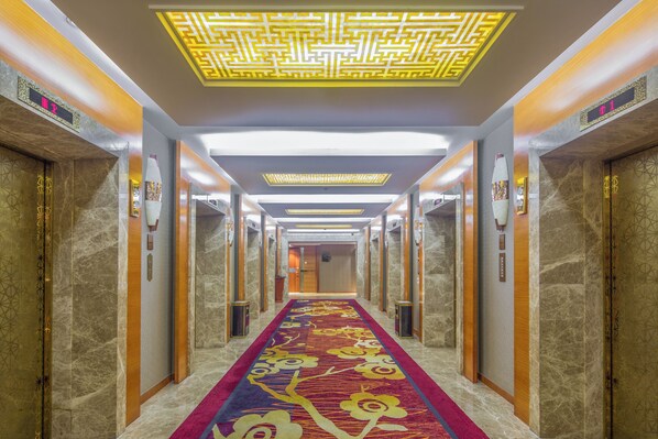 A hotel corridor with marble walls, a patterned carpet, and a modern ceiling design.