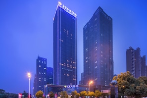 Un hotel de gran altura con señalización iluminada, rodeado de otros edificios altos y farolas.