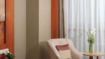 Une chambre d’hôtel avec un lit, une chaise, une petite table sur laquelle se trouve un vase de fleurs et un téléphone sur une table de chevet.