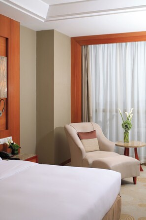 A hotel room with a bed, a chair, a small table with a vase of flowers, and a telephone on a nightstand.