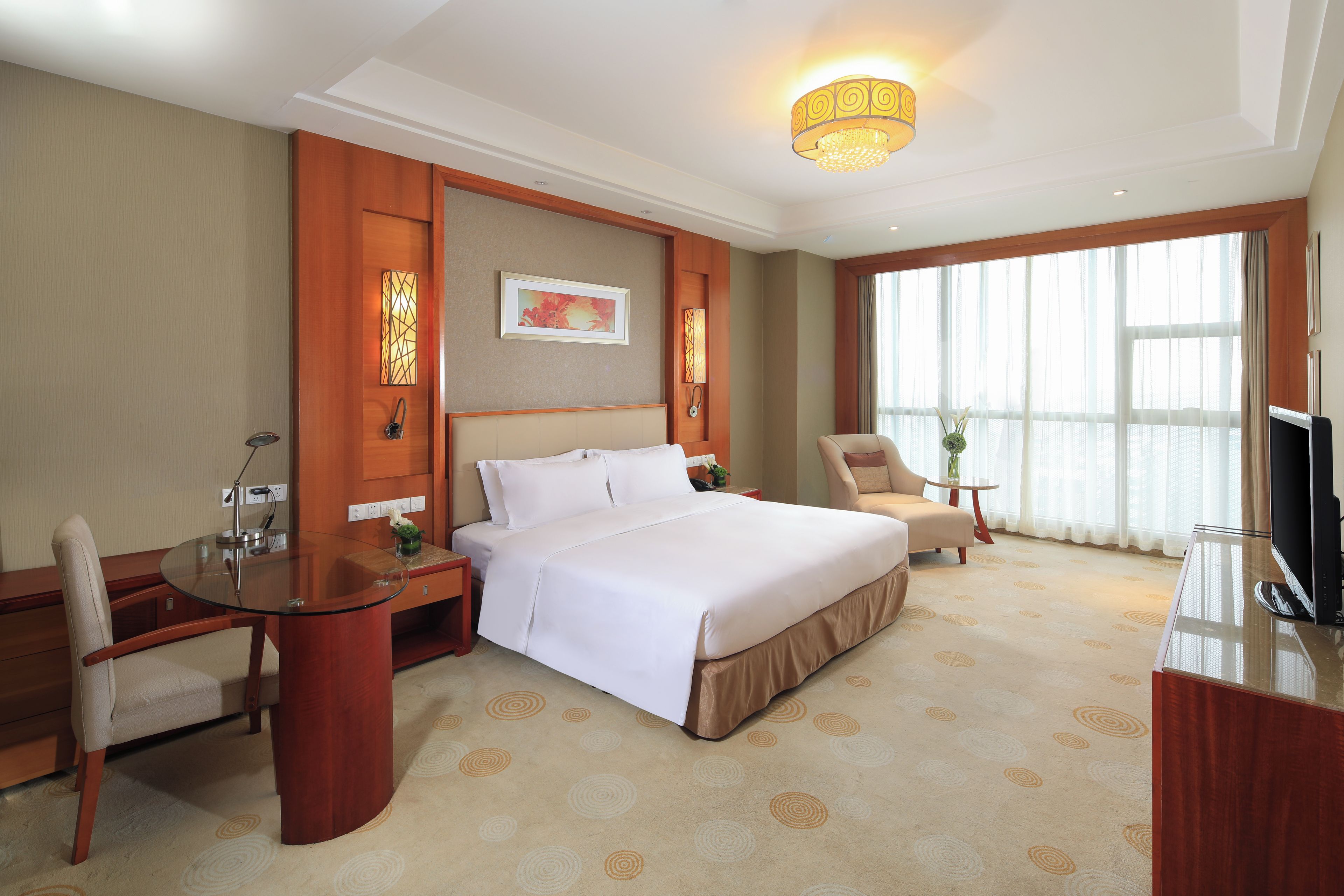 A hotel room with a bed, a desk, a chair, a television, and a large window.