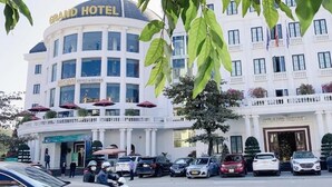 Un hotel con un llamativo letrero que dice 'Grand Hotel', un acceso cubierto y un estacionamiento con varios autos.