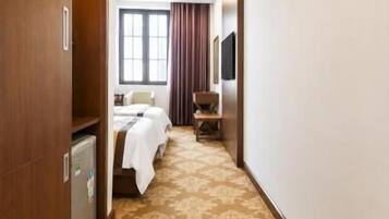 Ein Hotelgang mit einem gemusterten Teppich, einem Bett, einem Schreibtisch und einem Fernseher an der Wand.
