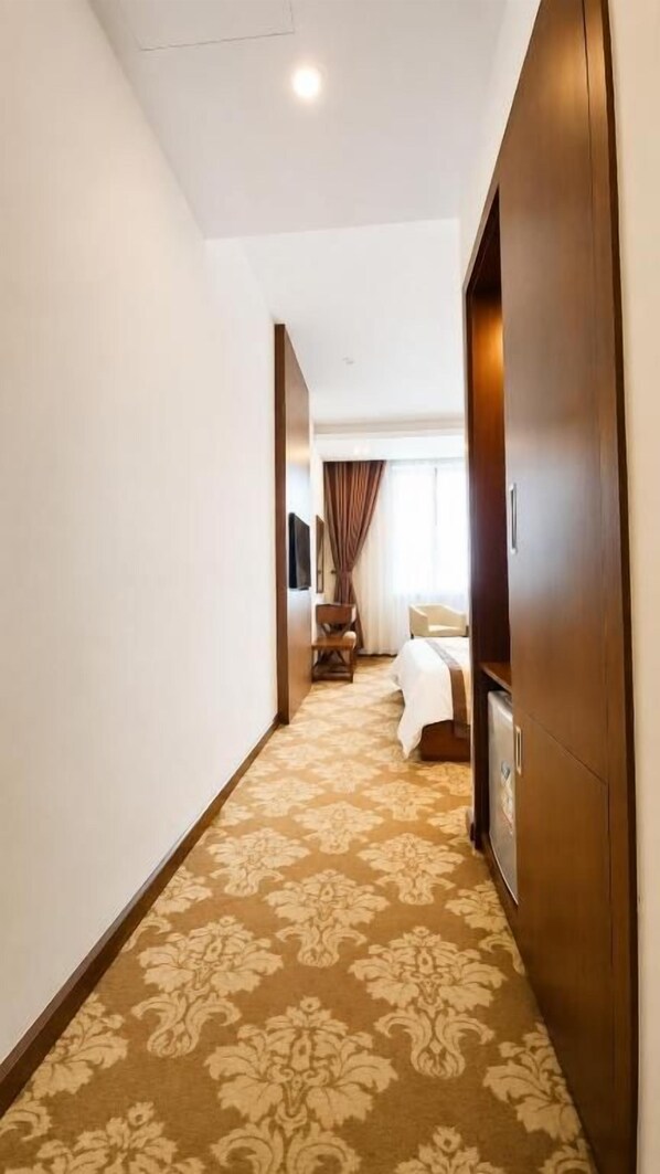 A hotel hallway with a carpeted floor, a bed, and a wardrobe.