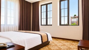 A hotel room with a large bed, a bedside table with a telephone, and a view of a building through the window.