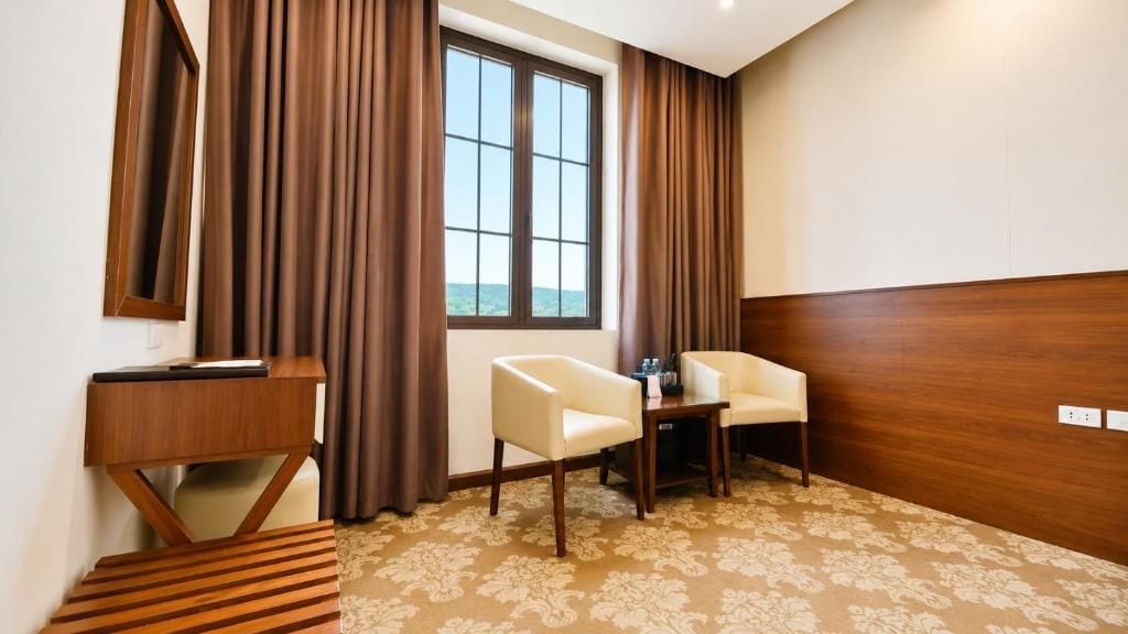 Ein Hotelzimmer mit großem Fenster, Schreibtisch aus Holz, Stuhl und kleinem Tisch.