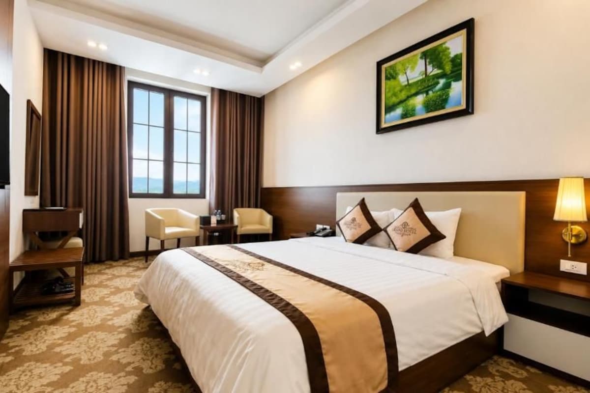 A hotel room with a large bed, a television, a desk, a chair, and a painting on the wall.