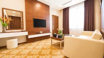 Ein Hotelzimmer mit einem an einer Holzwand montierten Flachbildfernseher, einem weißen Sofa, einem Couchtisch und einem gemusterten Teppich.