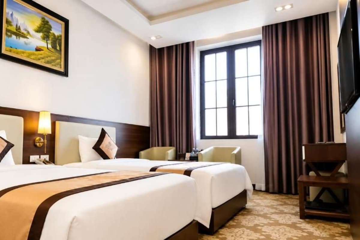 A hotel room with two beds, a desk, a chair, a television, and a painting on the wall.