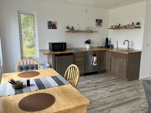 A modern kitchen with a dining area, wooden cabinetry, a built-in microwave, and a refrigerator. - Beautiful new and modern cabin with gorgeous Ninilchik River views. (Ninilchik)