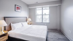 Una camera d'albergo moderna con un letto grande, due comodini con lampade, una finestra con tende e un quadro appeso al muro.