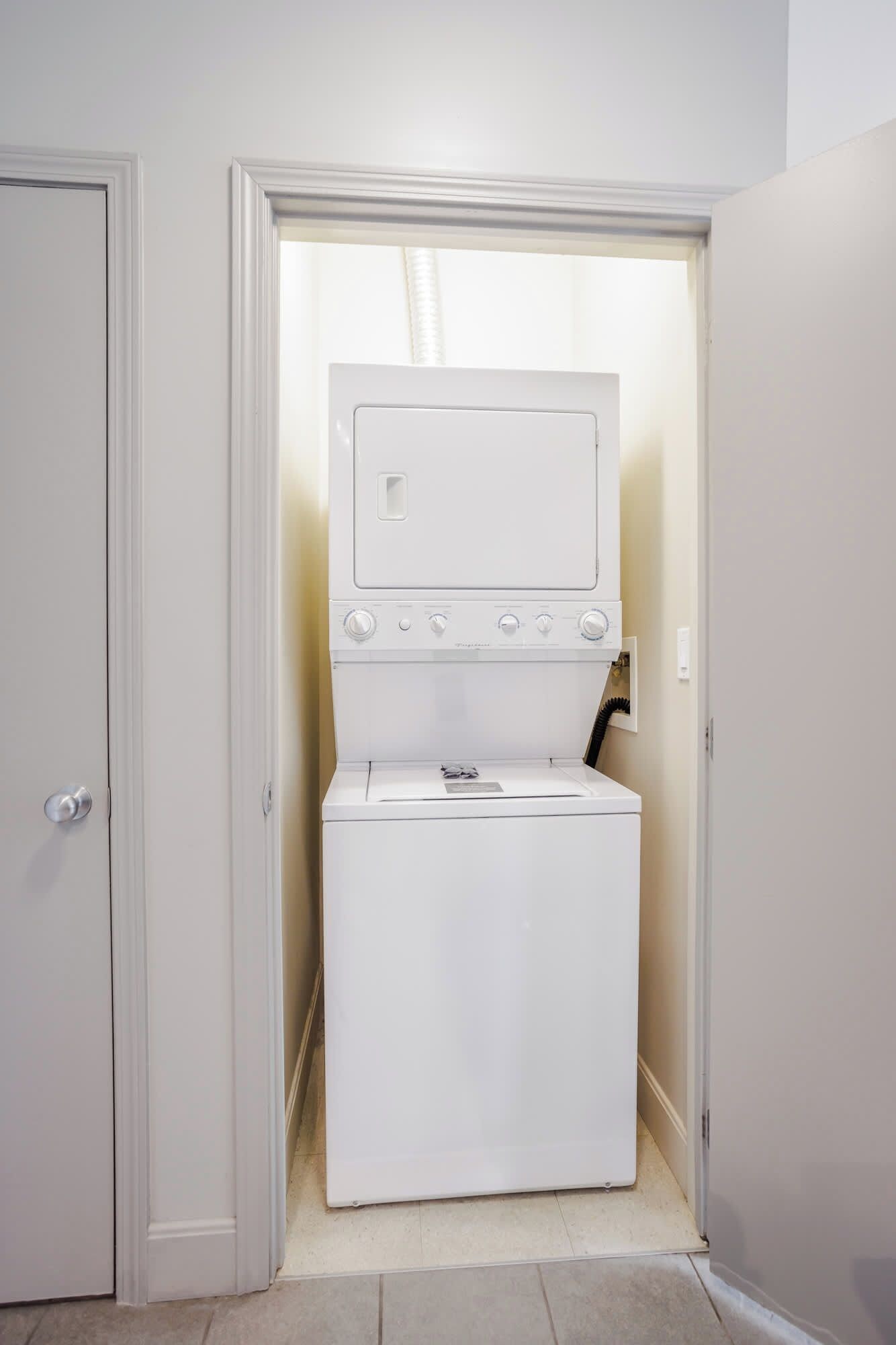 Une petite buanderie équipée d’un lave-linge et d’un sèche-linge à chargement frontal, d’une petite fenêtre et d’une porte donnant sur une autre pièce.