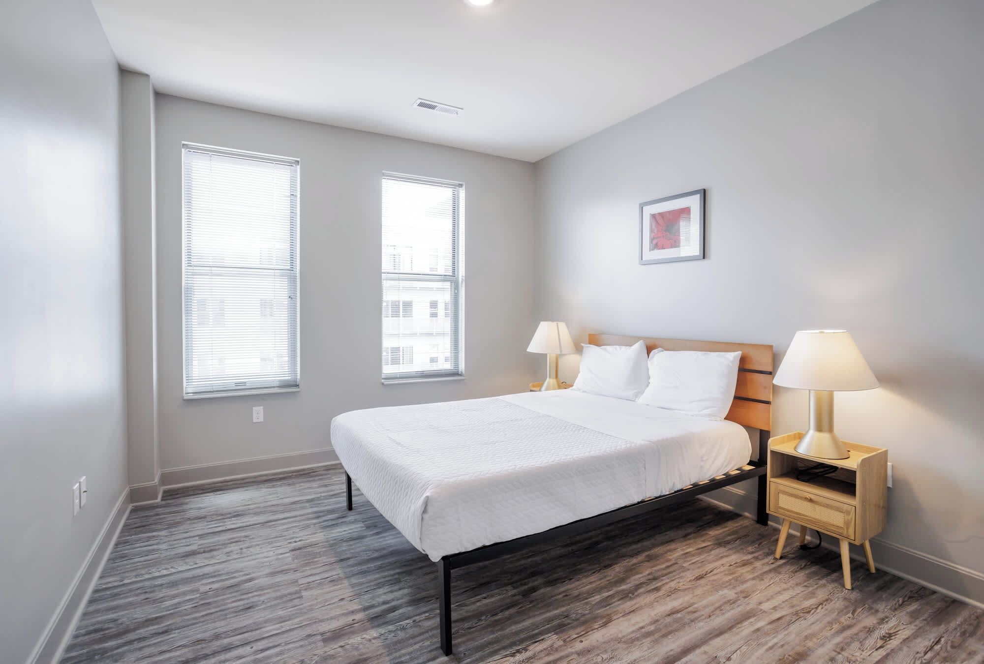 A bedroom with a bed, two bedside tables with lamps, and two windows.