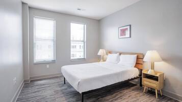 A bedroom with a bed, two bedside tables with lamps, and two windows.