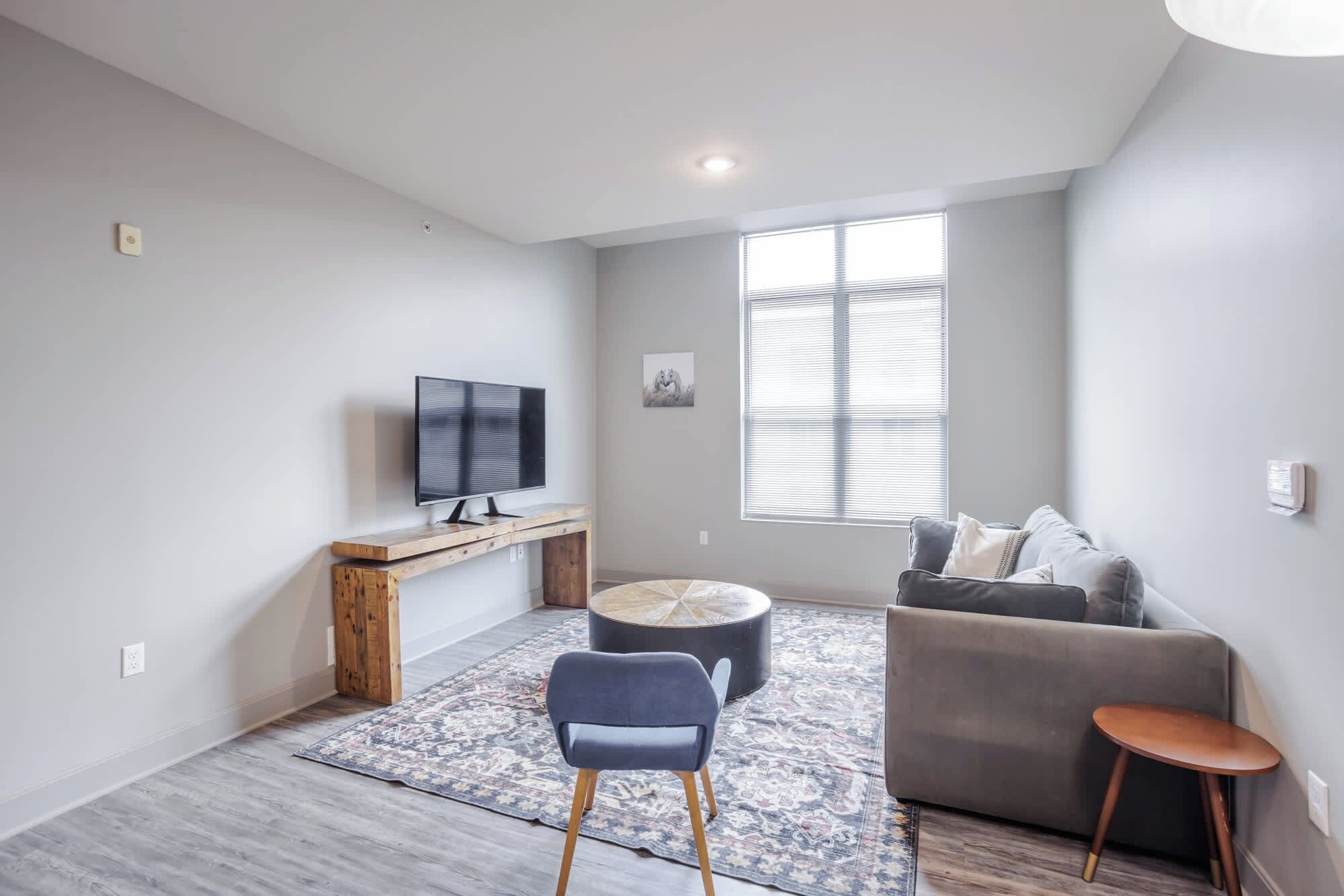 Ein modernes Wohnzimmer mit Flachbildfernseher, einem grauen Sofa, einem blauen Sessel und einem kleinen Holztisch.