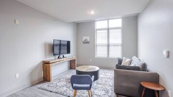 Ein modernes Wohnzimmer mit Flachbildfernseher, einem grauen Sofa, einem blauen Sessel und einem kleinen Holztisch.