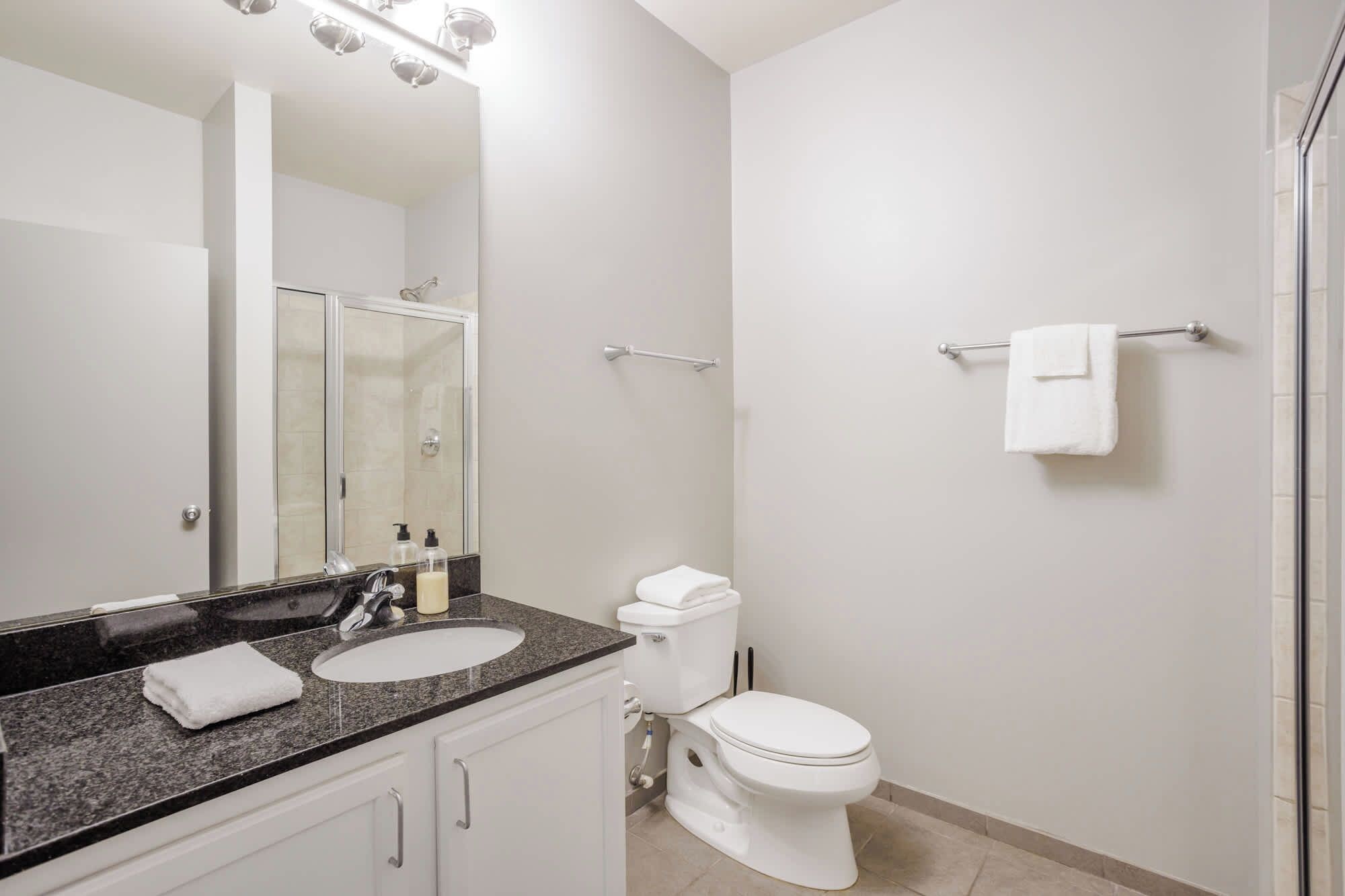 A modern bathroom with a double sink, a toilet, and a glass shower enclosure.