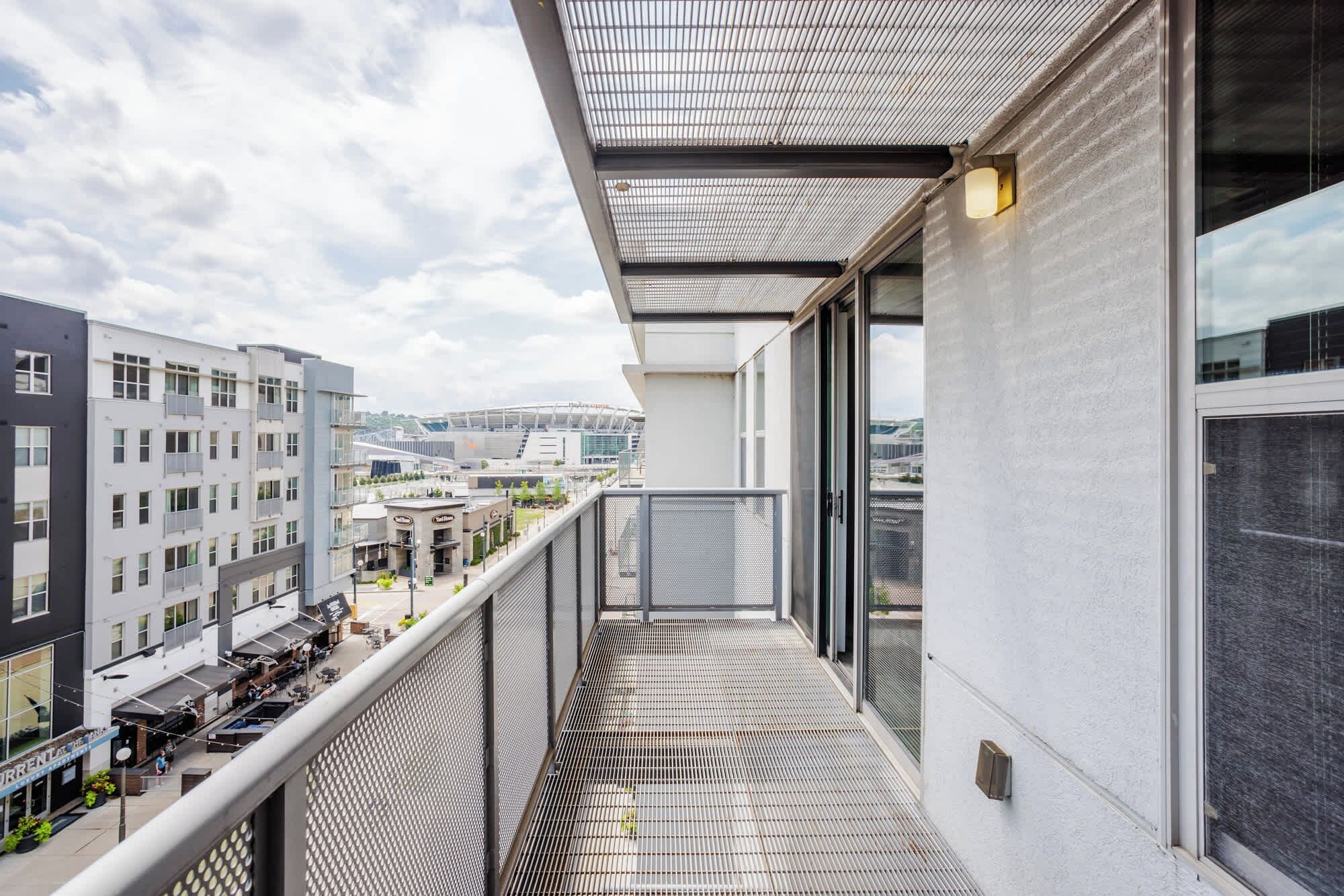 A balcony with a metal grid floor, overlooking a cityscape with buildings and a stadium.