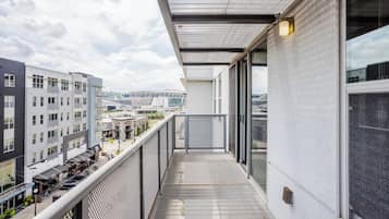 A balcony with a metal grid floor, overlooking a cityscape with buildings and a stadium.