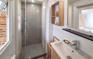 Ein modernes Badezimmer mit einer Duschkabine aus Glas, einem Waschbecken mit Seifenschale und einem Holzregal über dem Spiegel.
