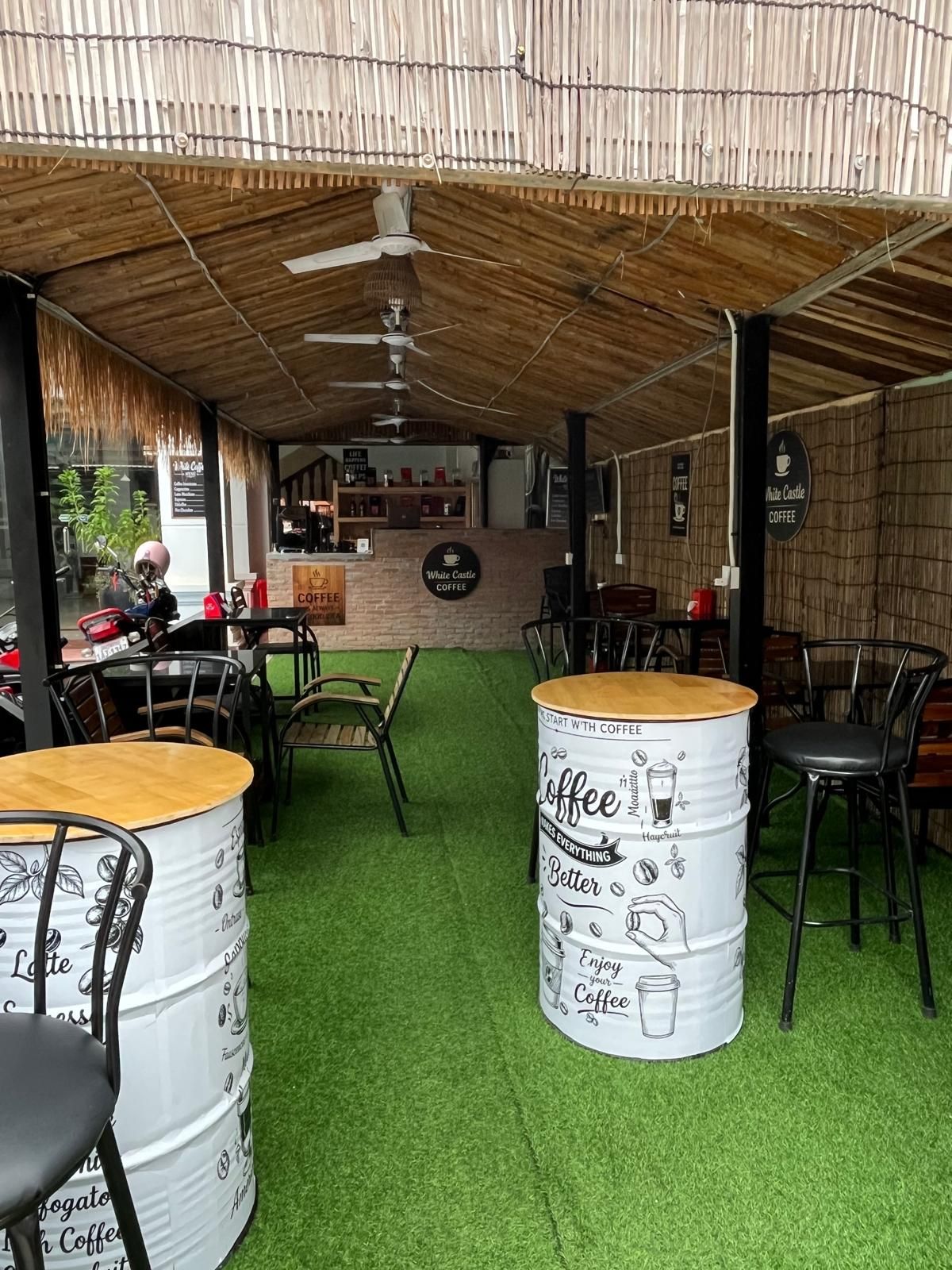 Un área exterior con mesas y sillas, una barra de café y una estructura con techo de paja.