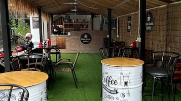 Un área exterior con mesas y sillas, una barra de café y una estructura con techo de paja.