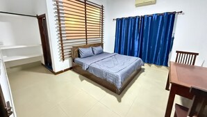 A bedroom with a bed, a window with blinds, a curtain, a table, and a chair. - White Castle (Krong Siem Reap)