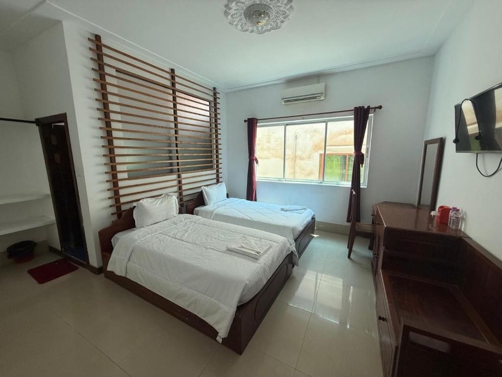 Un dormitorio con dos camas, cabecero de madera, televisor y ventana con cortinas.