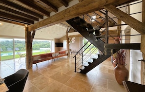 A spacious room with a large window, a staircase, and a view of a pool. - Superbe maison avec piscine (Lanneplaà)