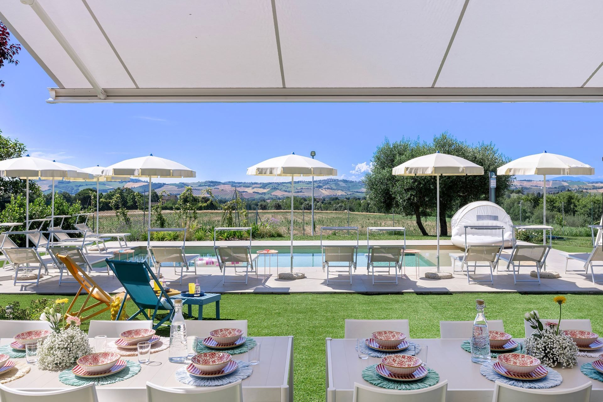 Ein Poolbereich im Freien mit Liegestühlen und Sonnenschirmen, Essbereich mit Tischen und Stühlen sowie Blick auf die Landschaft.