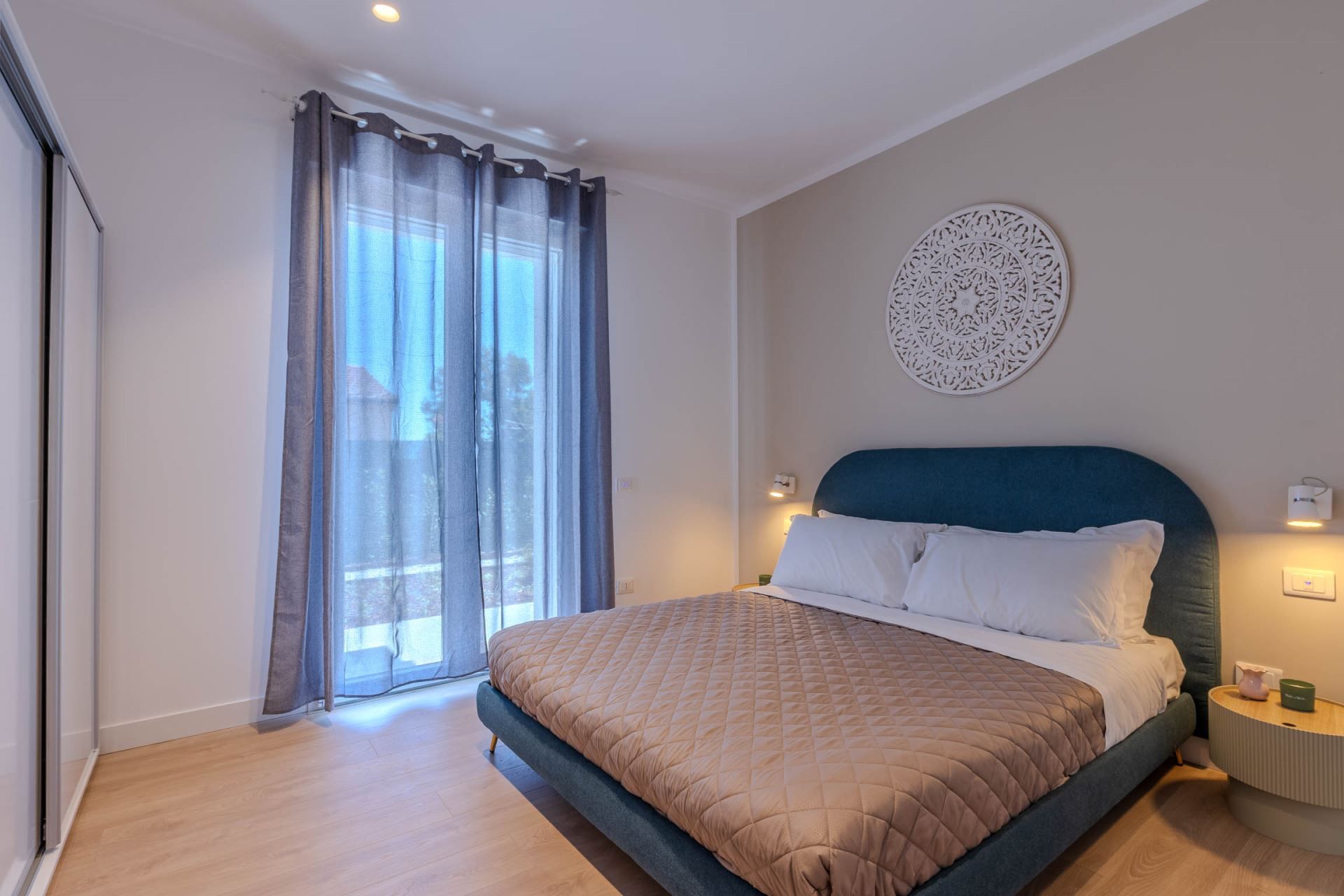 Una camera da letto con un letto, un decoro rotondo a parete, un comodino e una finestra con tende.
