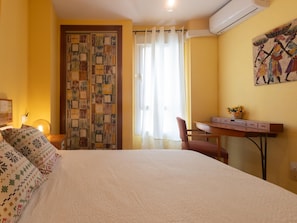 Habitació d'hotel amb llit, escriptori, cadira, finestra amb cortines i aire condicionat fixat a la paret.