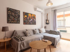 Un saló modern amb un sofà gris, dos quadres, una guitarra i una taula de fusta petita.