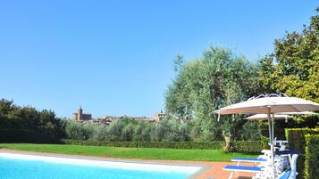 A swimming pool with lounge chairs and an umbrella, surrounded by greenery and a view of a historic building.