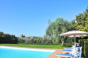A swimming pool with lounge chairs and an umbrella, surrounded by greenery and a view of a historic building.