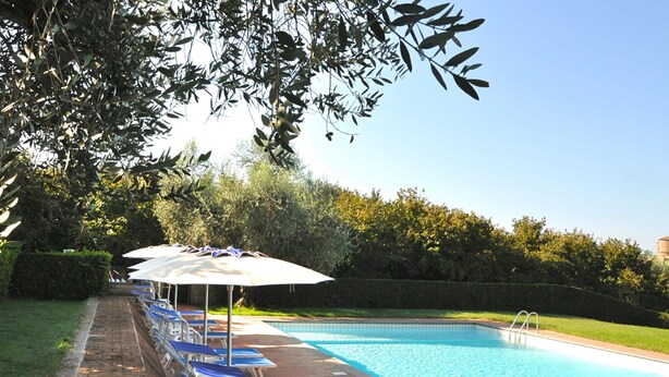 Una piscina con lettini e ombrelloni, immersa nel verde.
