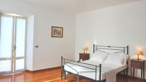 Una camera da letto con una struttura letto in metallo, due comodini con lampade, un letto singolo con biancheria da letto bianca, un pavimento in legno, una porta con pannelli in vetro satinato e un quadro appeso al muro.