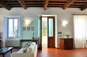A living room with a sofa, a coffee table, a radiator, a television, and a door leading outside.