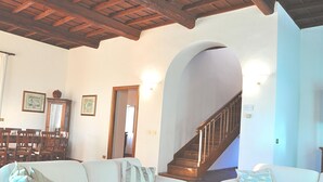 Un soggiorno con soffitto in legno, una scala e un'area pranzo con sedie e tavolo.