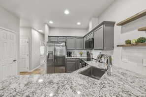 A modern kitchen with stainless steel appliances, a granite countertop, and white cabinetry. - The Donnelly Den | Tamarack Getaway, Game Room (Donnelly)